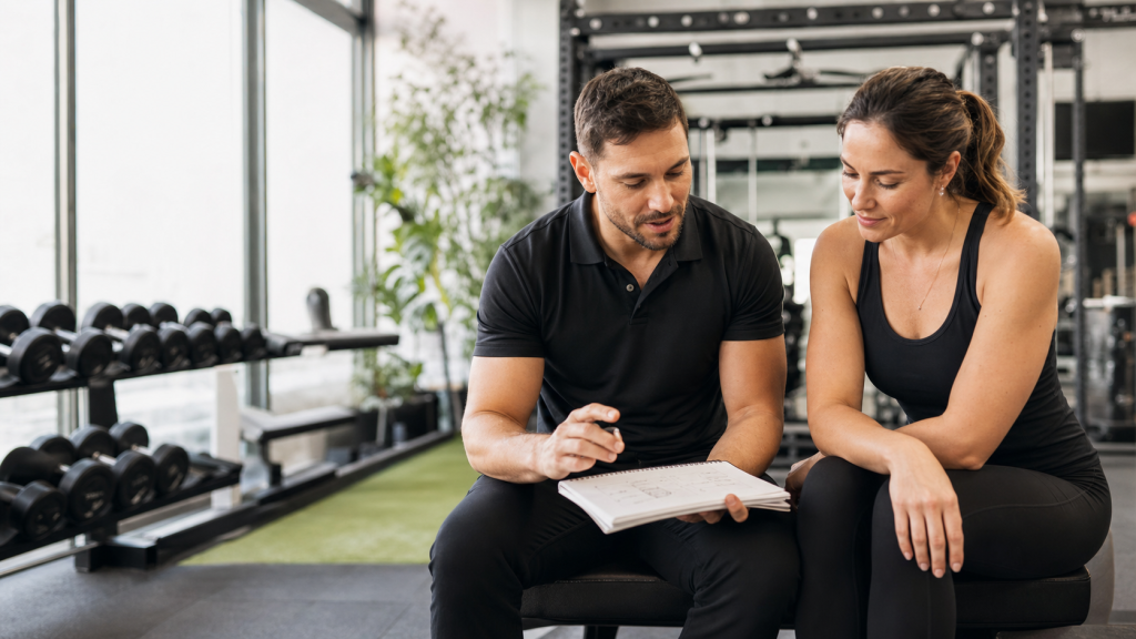 Coach sportif professionnel échangeant avec un client dans une salle de sport moderne pour choisir une offre d’accompagnement adaptée